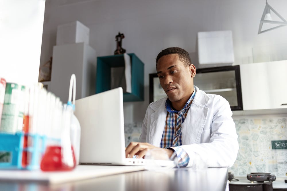 A man in a lab coat types on a computer
