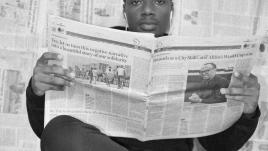 Homme lisant un journal devant un mur de journaux