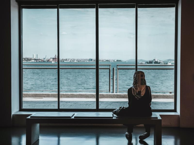 Woman sits alone looking out a large window