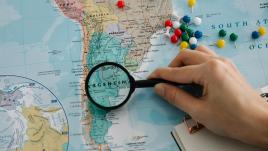 A map of Latin America and a person holding a magnifying glass over Argentina.
