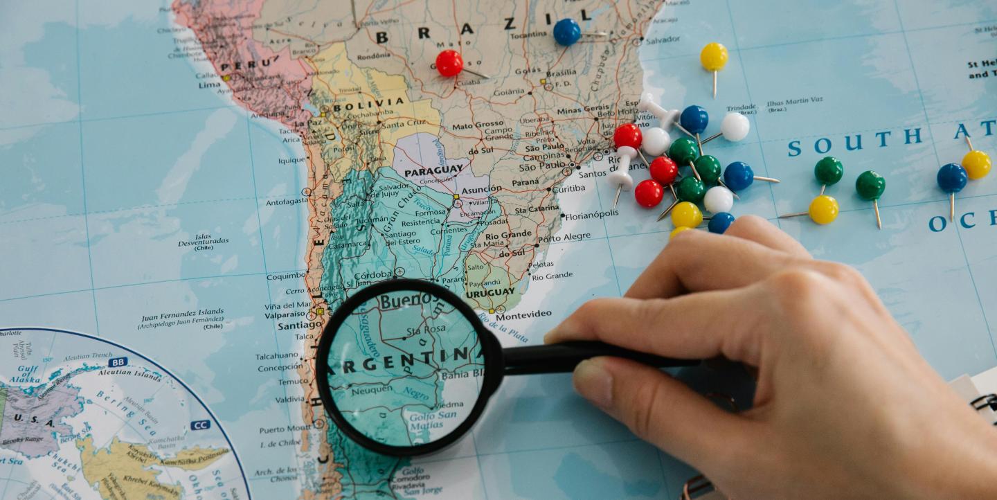 A map of Latin America and a person holding a magnifying glass over Argentina.