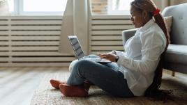 A woman sitting on the floor and working on her laptop. 