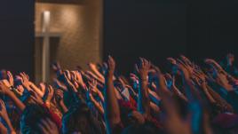 People at church with their hands up and a cross in the background.